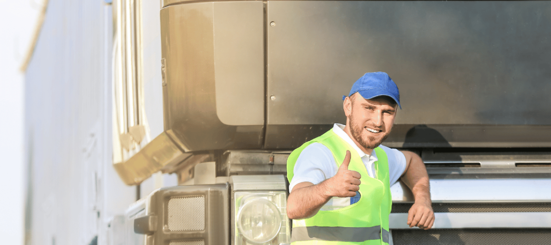 a hgv driver stands in front of his cab smiling and thumb held up