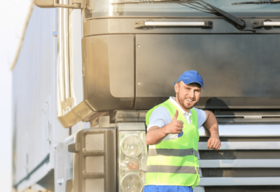 a hgv driver stands in front of his cab smiling and thumb held up